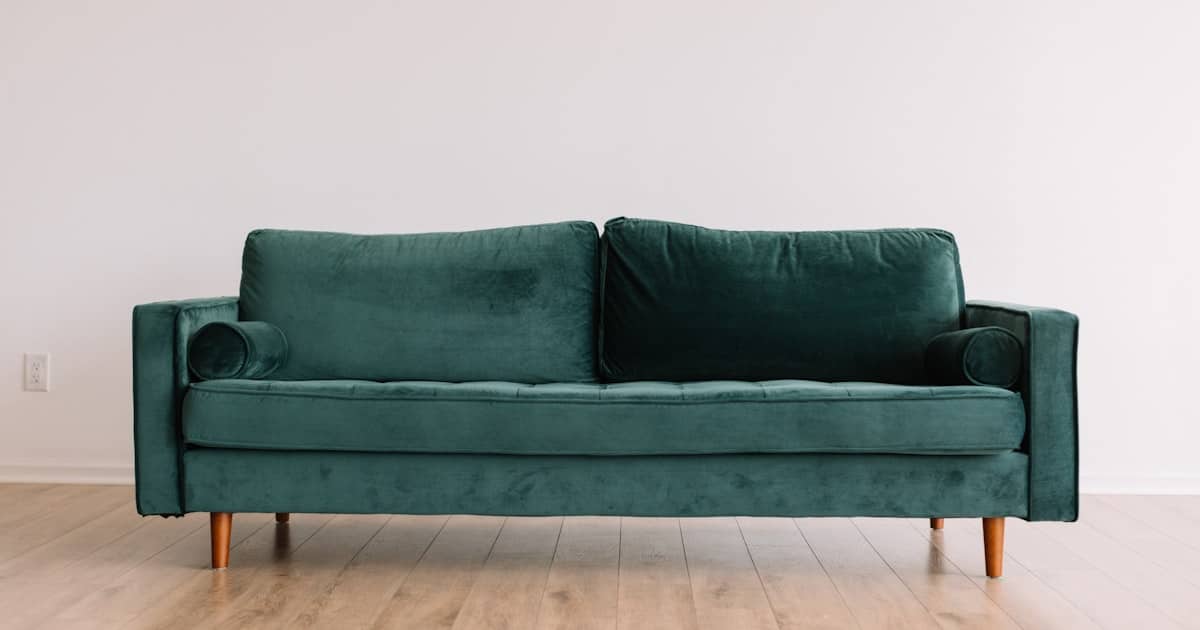 Ormau mid-century modern emerald green velvet sofa with bolster pillows and tapered wooden legs.